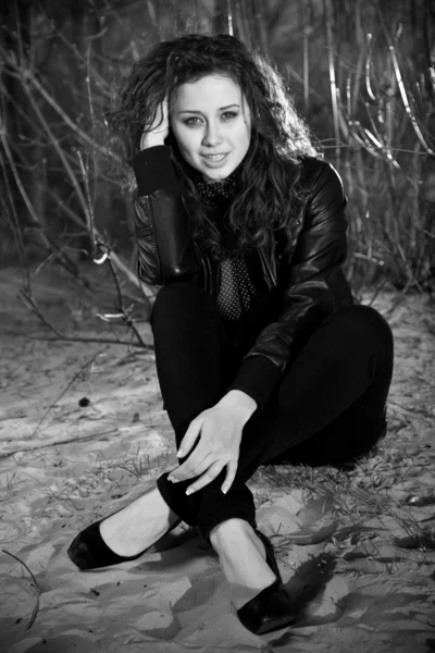 Woman in leather jacket sitting on sand with crossed legs — Stock Photo, Image