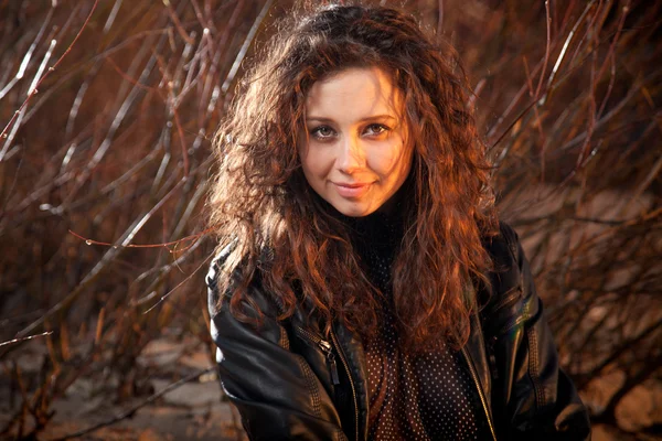 Portrait de femme bouclée souriante en manteau de cuir contre la forêt — Photo