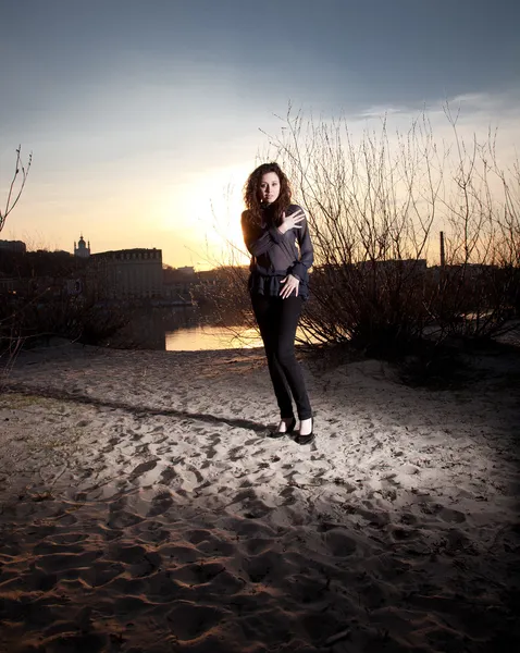 Donna in abiti alla moda in piedi sulla spiaggia al tramonto — Foto Stock