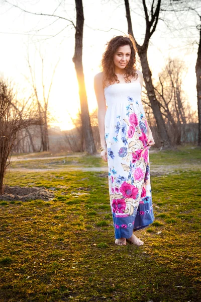 Jonge vrouw in jurk lopen op weide bij zonsondergang — Stockfoto