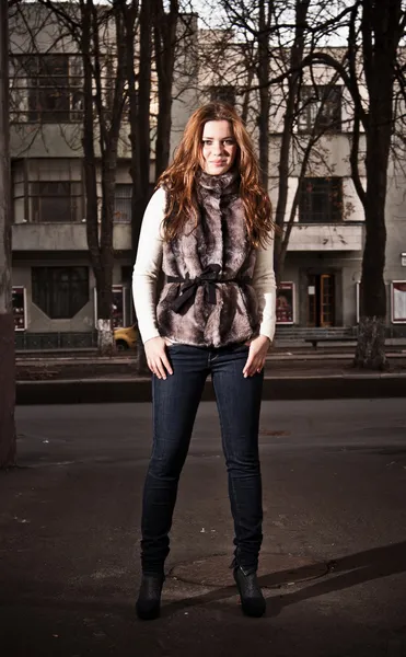 Femme rousse en manteau de fourrure et jeans debout dans la rue — Photo