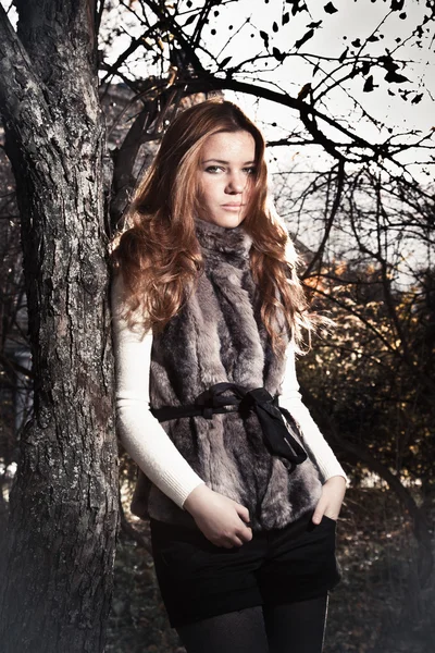 Frau im Pelzmantel lehnt im Park an altem Baum — Stockfoto