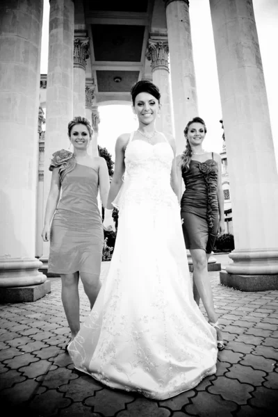 Braut geht mit zwei Brautjungfern gegen antike Säulen — Stockfoto