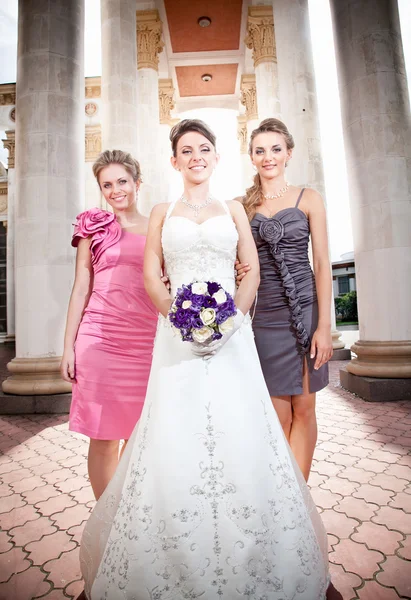 Bride with two bridesmaids against colonnade — Stock Photo, Image