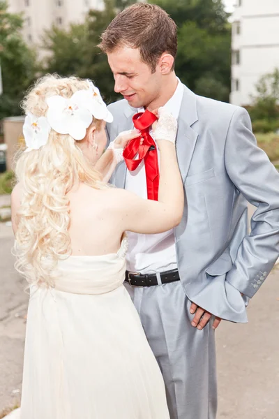 Blonde bruid koppelverkoop rode stropdas op bruidegom — Stockfoto