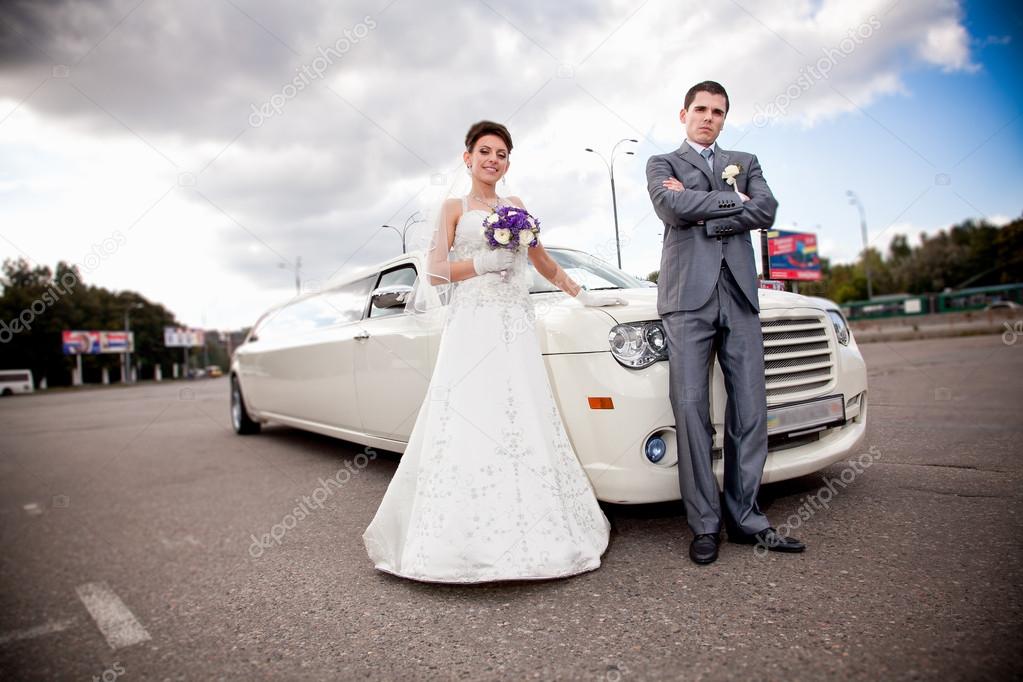 Just married couple standing against long white limousine
