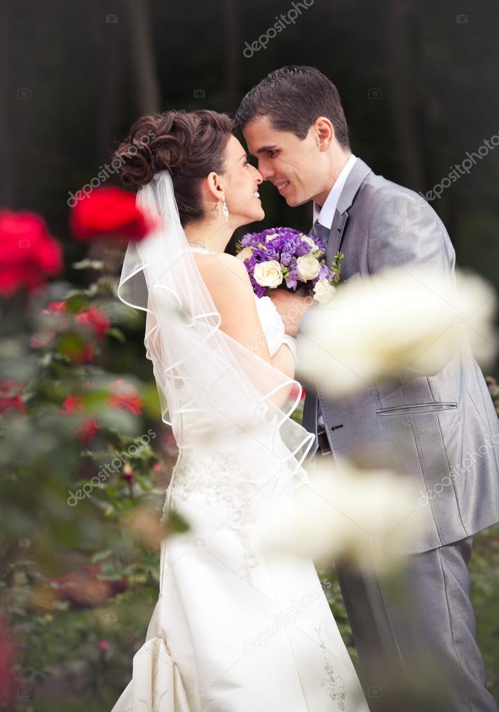 Newly married couple looking at each other in garden with roses