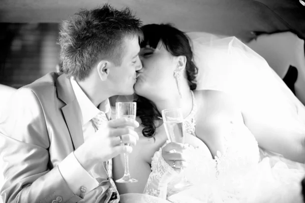 Newly married couple holding glasses and kissing at car — Stock Photo, Image