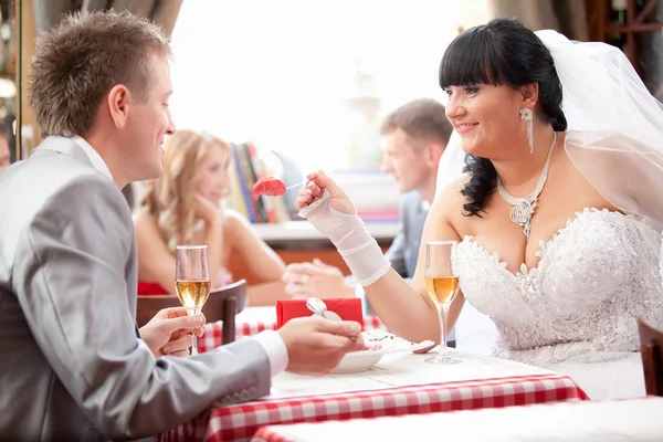Brunette bride feeding groom from spoon at restaurant — Stock Photo, Image