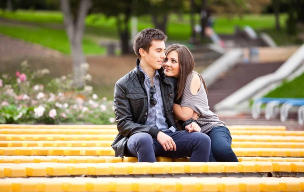 Namoro casal abraçando no banco amarelo no parque — Fotografia de Stock