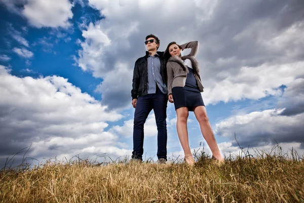 Casal elegante posando no campo contra o céu azul — Fotografia de Stock