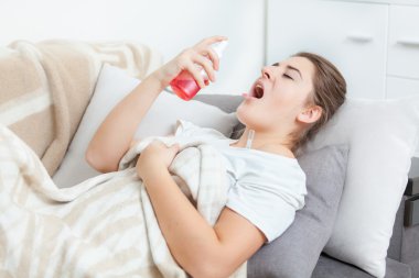 Woman using throat spray while lying on couch