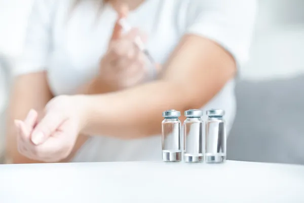 Tiro de frascos de vidrio con insulina contra mujer haciendo pinchazo — Foto de Stock