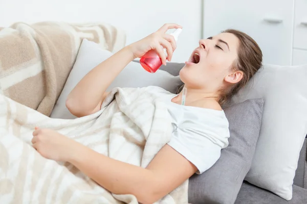 Sick woman lying in living room and using throat spray — Stock Photo, Image