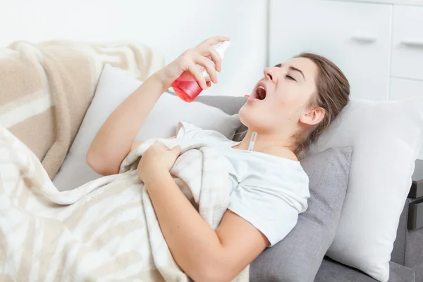 Woman using throat spray while lying on couch — Stok fotoğraf