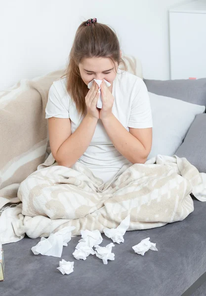 Young woman sitting on couch and blowing nose — Stock Photo, Image