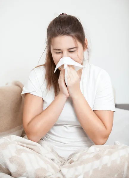 Brunette woman sitting on bed and sneezing — Stock Photo, Image