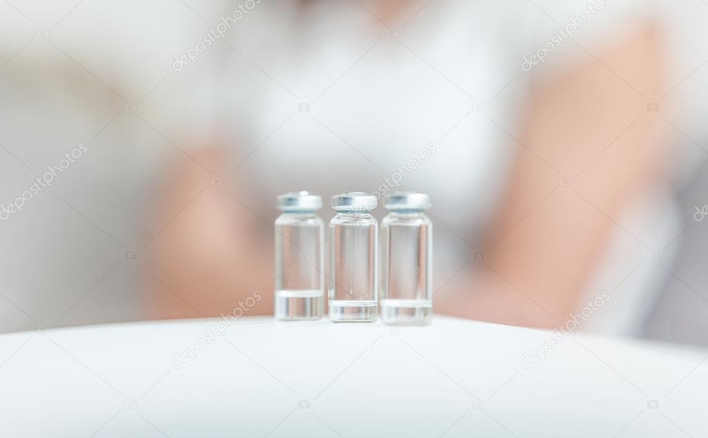 Ampules with medicines standing on table against sitting patient
