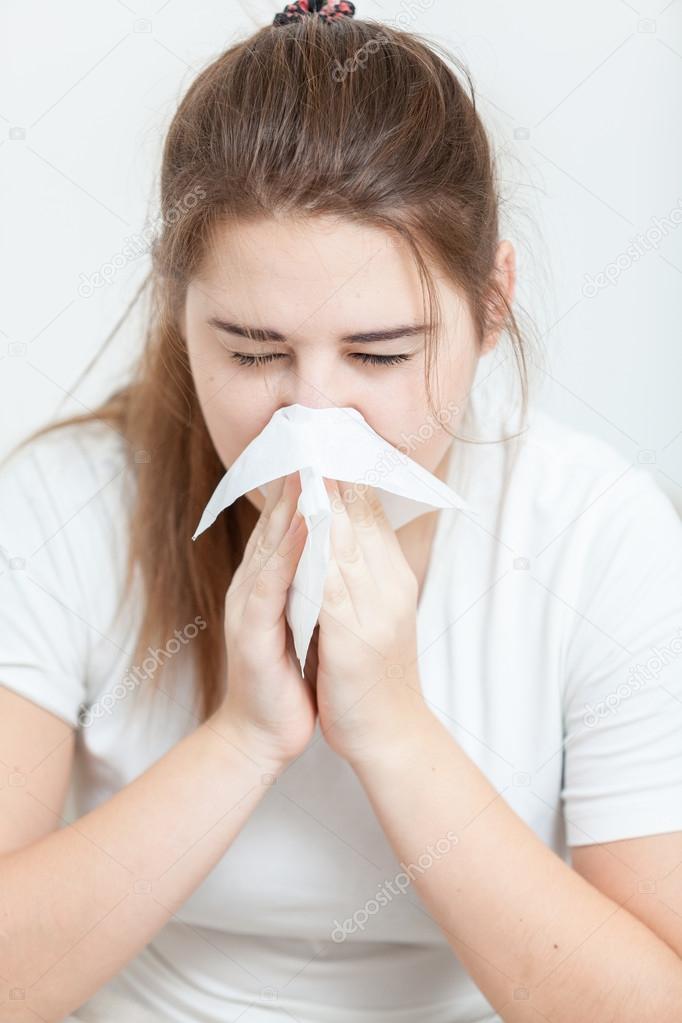 Portrait of sick brunette girl sneezing in paper tissue