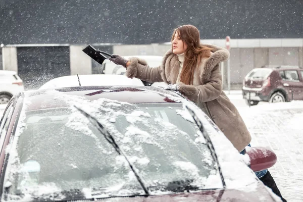 Young woman cleaning snow from car roof using brush — Stock Photo, Image