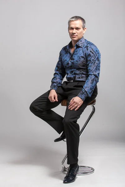 Man in blue shirt sitting on high chair against white background