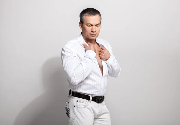 Adult man unbuttoning white shirt against white background — Stock Photo, Image