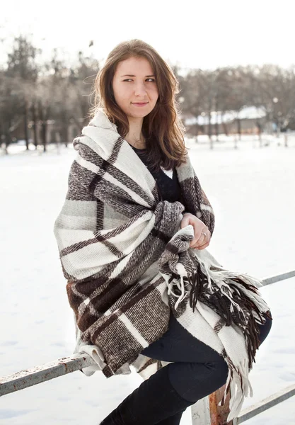 Smiling woman in plaid sitting on wooden fence at winter — Stock Photo, Image