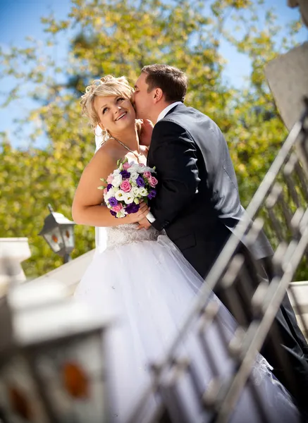 Newly married couple kissing on porch against green trees — Stock Photo, Image