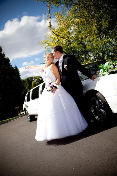 Newly married couple hugging against white limousine — Stock Photo, Image