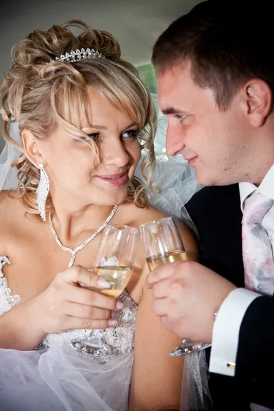 Casamento recém-casado casal clinking óculos no banco de trás da limusine — Fotografia de Stock