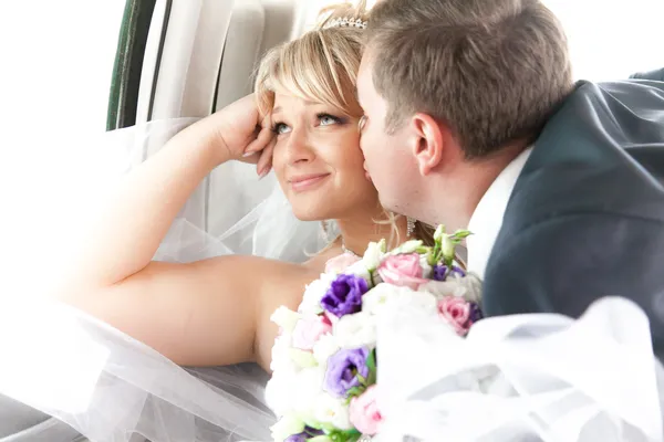 Young groom kissing smiling bride on backseat — Stock Photo, Image