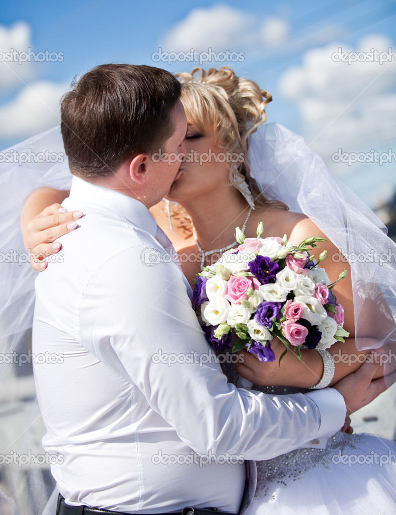 Newly married couple kissing against blue sky
