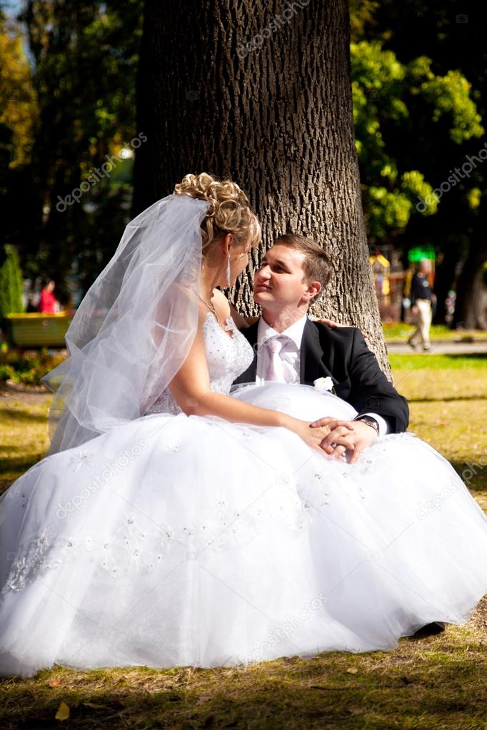 Bride sitting on grooms legs under tree at park