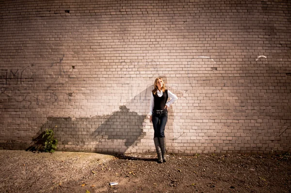 Blonde woman leaning against long tiled wall on street — Stock Photo, Image