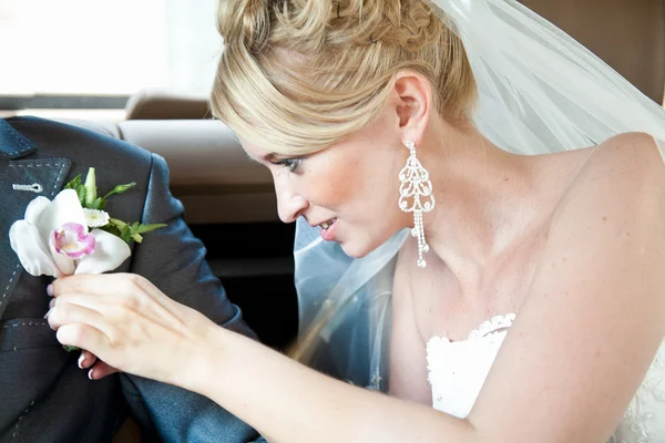 Blond bride attaching boutonniere on husbands jacket — Stock Photo, Image