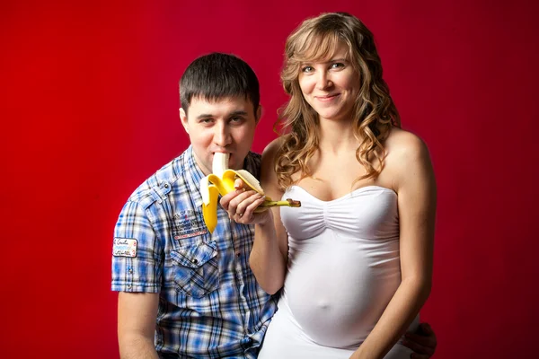 Pregnant woman in white dress feeding husband with banana — Stock Photo, Image