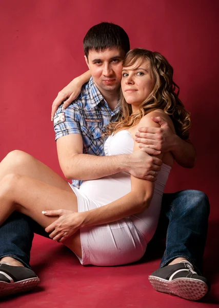 Pregnant woman lying with husband on red background — Stock Photo, Image