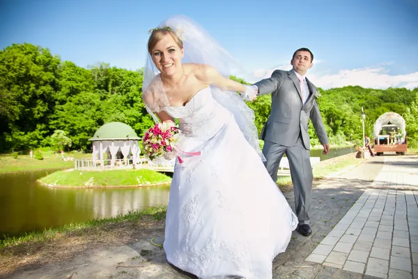 Bruid trekken knappe bruidegom met de hand in het park — Stockfoto