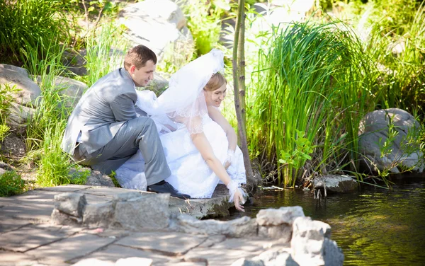 Супружеская пара, сидящая на берегу реки и касающаяся воды — стоковое фото