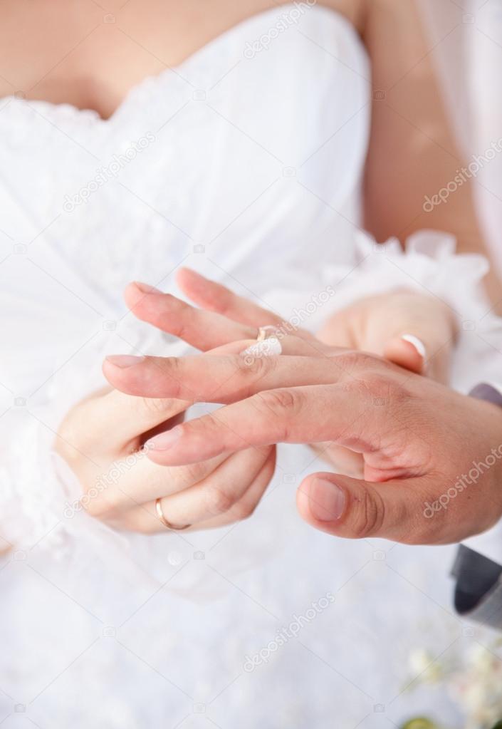 Bride in white dress putting wedding ring on grooms finger
