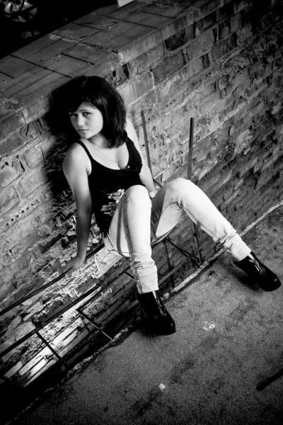 Sexy brunette woman sitting on street leaning against wall — Stock Photo, Image