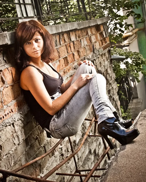 Brunette girl sitting on street against old brick wall Royalty Free Stock Photos