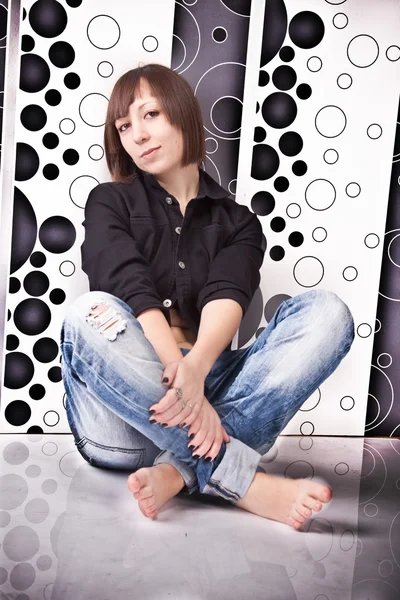 Woman in jeans and shirt sitting on floor against fancy wall — Stock Photo, Image