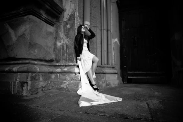 Mulher de vestido branco longo encostado contra a parede de pedra — Fotografia de Stock