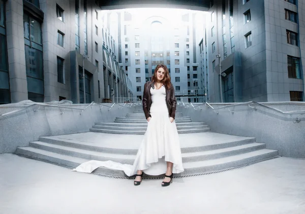 Mujer en vestido blanco largo de pie en las escaleras contra el edificio moderno — Foto de Stock