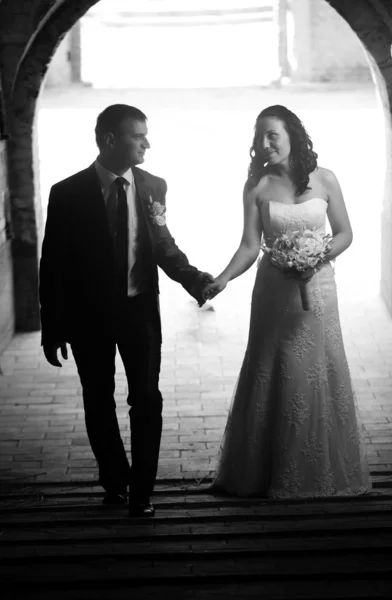 Foto di sposa e sposo che camminano sotto il grande vecchio arco — Foto Stock