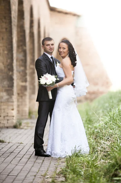 Portrait of bride and groom hugging under tall brick castle wall — Stock Photo, Image