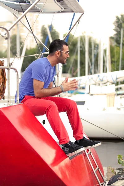 Hombre latino sentado en la cubierta de yate rojo en el puerto —  Fotos de Stock