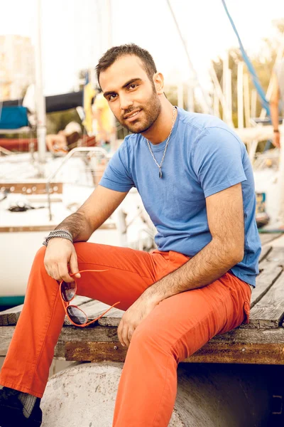 Retrato del hombre guapo sentado en el muelle contra yates —  Fotos de Stock