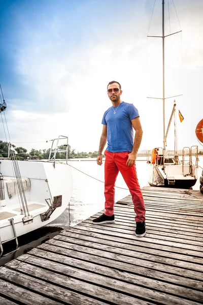 Retrato de un hombre guapo parado en el muelle contra yates blancos — Foto de Stock